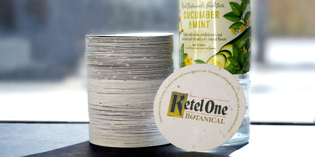 stack of plantable coasters next to bottle of vodka with one coaster leaning against bottle